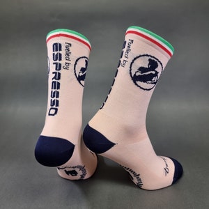 May include: A pair of pink athletic socks with a navy blue toe and heel. The socks have a white and green stripe at the top and feature the text "Fuelled by Espresso" and a logo of a person drinking coffee.