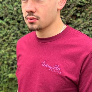 May include: A maroon t-shirt with a purple logo that says "tranquillo cycling" on the front.