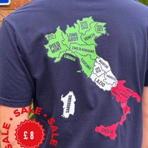 May include: A navy blue t-shirt featuring a large graphic on the back of the Italian peninsula divided into three colour sections. The northern regions are green, the central regions are white, and the southern regions are red, with labels for each.
