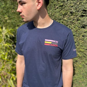 May include: A navy blue t-shirt with a colourful graphic design on the front. The graphic features the words "Vai Allez Vamos" in a retro style.