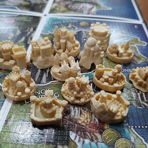 Può includere: Una collezione di 12 strutture in miniatura a forma di castello in plastica beige. Le strutture sono disposte su una scacchiera con una mappa di una terra immaginaria.