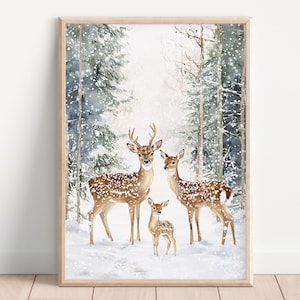 May include: A framed watercolour print depicting a deer family in a snowy woodland scene. The image shows a buck with antlers, two does, and a fawn, all with brown and white spotted coats. The background features snow-covered trees and a wintery atmosphere.