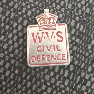 Puede incluir: Una insignia de metal plateado y rojo con una corona en la parte superior y el texto "W.V.S. CIVIL DEFENCE".