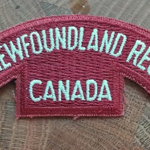 Op de afbeelding: Een gebogen rode patch met witte geborduurde tekst die "Royal Newfoundland Regiment Canada" luidt.
