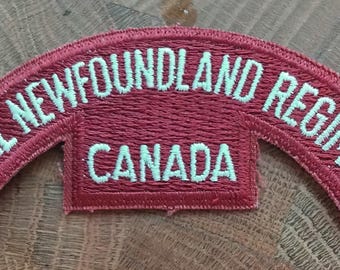 May include: A red curved patch with white embroidered text that reads "Royal Newfoundland Regiment Canada".