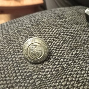 Puede incluir: Un botón plateado con las palabras "KINGHATH" y un escudo con un pájaro y una estrella.