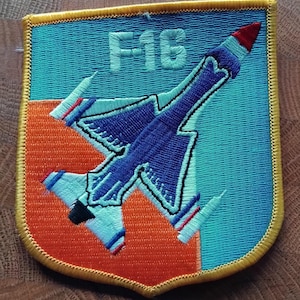 May include: An embroidered patch featuring a fighter jet in blue and orange with the text "F16" in white.
