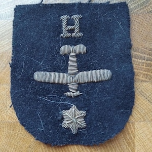 May include: A dark blue fabric patch with a silver embroidered airplane, a silver embroidered letter "H", and a silver embroidered star.