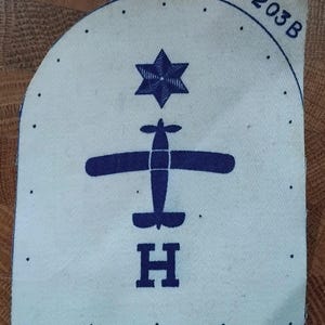 May include: A blue and white embroidered patch with a star of David, a small airplane, and the letter "H" below it. The number "203B" is in the upper right corner.