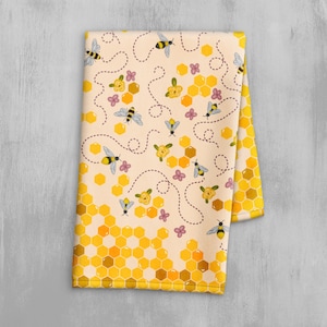 Op de afbeelding: Een gele en witte keukendoek met een patroon van bijen, honingraten en bloemen.