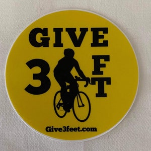 May include: Yellow round sticker with black text that reads "GIVE 3 FT" and a silhouette of a person riding a bicycle. The text "Give3feet.com" is at the bottom of the sticker.