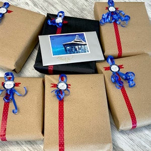May include: Seven brown paper wrapped gifts with red and white polka dot ribbon and blue ribbon bows. Each gift has a round blue sticker with white text. One gift is wrapped in black paper with a red ribbon and a card with a picture of a boat and the text "Thank You!"