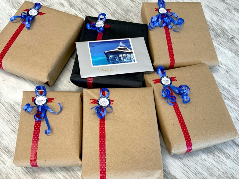 May include: Seven brown paper wrapped gifts with red and white polka dot ribbon and blue ribbon bows. Each gift has a round blue sticker with white text. One gift is wrapped in black paper with a red ribbon and a card with a picture of a boat and the text "Thank You!"