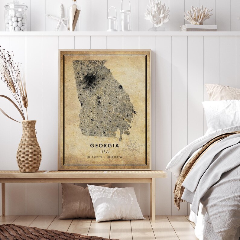 May include: A framed map of Georgia, USA, with a vintage aesthetic. The map is in shades of beige and black, with the state's outline and city details visible. The text "GEORGIA USA" and coordinates are at the bottom. The frame is a light brown color.