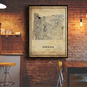 Puede incluir: Un mapa enmarcado de Oreg&oacute;n, EE. UU., con una est&eacute;tica vintage. El mapa est&aacute; en tonos grises y beige, con el contorno del estado en un lugar destacado. El texto "Oregon USA" y las coordenadas est&aacute;n debajo.