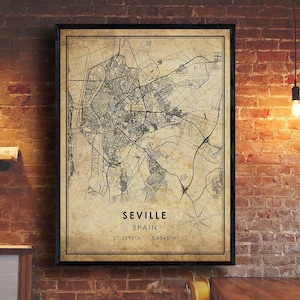 May include: A framed map print of Seville, Spain, in a vintage style. The map features detailed street layouts and geographical coordinates. The print is in a black frame and hangs on a brick wall.