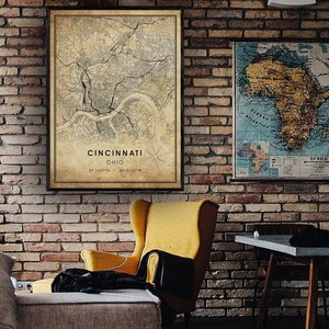 May include: A vintage-style map of Cincinnati, Ohio, framed in black, hangs on a brick wall. The map shows the city's streets and landmarks. The map is titled "Cincinnati, Ohio" and includes the coordinates "39.1031&deg;N, 84.5120&deg;W".