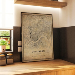 May include: A vintage-style map print of Cincinnati, Ohio, with a brown background and black lines depicting streets and waterways. The text "Cincinnati, Ohio, 39.1031&deg;N, 84.5120&deg;W" is printed at the bottom of the map.
