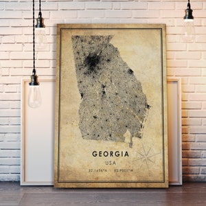 May include: A framed map of Georgia, USA, with a vintage aesthetic. The map is detailed with a network of lines and dots, and the state's outline is prominent. The text "GEORGIA USA" and coordinates are printed at the bottom. A compass rose is in the lower right corner.