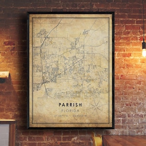 May include: A framed map print of Parrish, Florida, with coordinates 27.5877°N 82.4255°W. The map has a vintage aesthetic with a sepia tone and a compass rose. The frame is black, and the print is hanging on a brick wall.