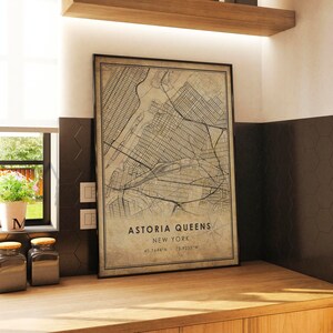 May include: A vintage-style map print of Astoria, Queens, New York City. The map is framed in a black frame and has a beige background with black lines showing the streets and waterways. The text "Astoria Queens, New York, 40.7664&deg;N, 73.9235&deg;W" is printed at the bottom of the map.