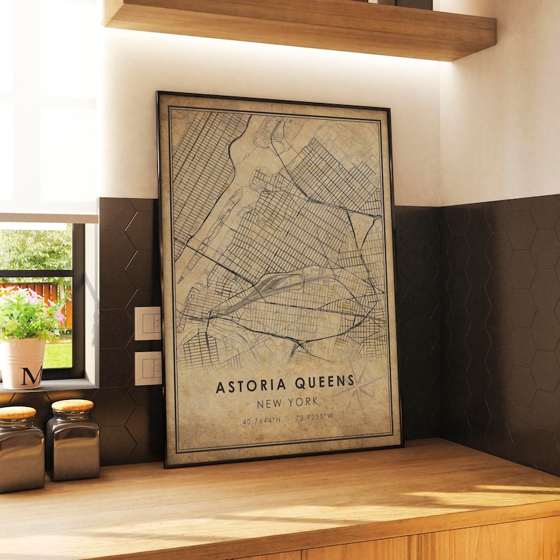 May include: A vintage-style map print of Astoria, Queens, New York City. The map is framed in a black frame and has a beige background with black lines showing the streets and waterways. The text "Astoria Queens, New York, 40.7664&deg;N, 73.9235&deg;W" is printed at the bottom of the map.