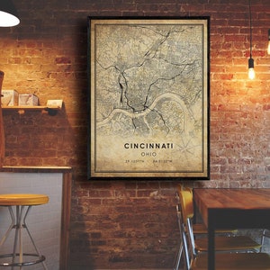 May include: A vintage-style map print of Cincinnati, Ohio, with a black frame. The map shows the city's streets and landmarks. The text "Cincinnati, Ohio" and the coordinates "39.1031&deg;N - 84.5120&deg;W" are printed below the map.