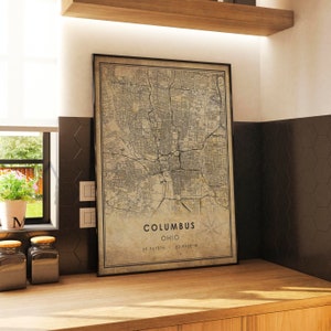 May include: A vintage-style map print of Columbus, Ohio. The map is in black and white and shows the city's streets and landmarks. The text "Columbus, Ohio" and the coordinates "39.9612&deg;N 82.9988&deg;W" are printed at the bottom of the map.
