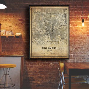 May include: A vintage-style map print of Columbus, Ohio. The map is printed on a beige background with black lines and text. The city name and coordinates are printed in black at the bottom of the map.
