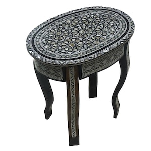 May include: A small oval table with a black and white inlaid design. The table has three legs and a drawer. The table is made of wood and has a black finish.