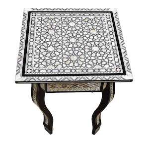 May include: A small, square, black and white table with intricate inlaid mother-of-pearl designs. The table has four legs with a curved design.
