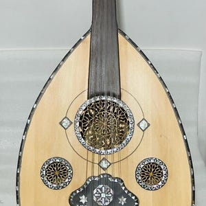 Op de afbeelding: Een lichtgekleurde oed, een snaarinstrument uit het Midden-Oosten, met een peervormige body. Het instrument heeft ingewikkelde inlegwerk van parelmoer rond de klankgaten en randen. De hals en stemschroeven zijn van donker hout.