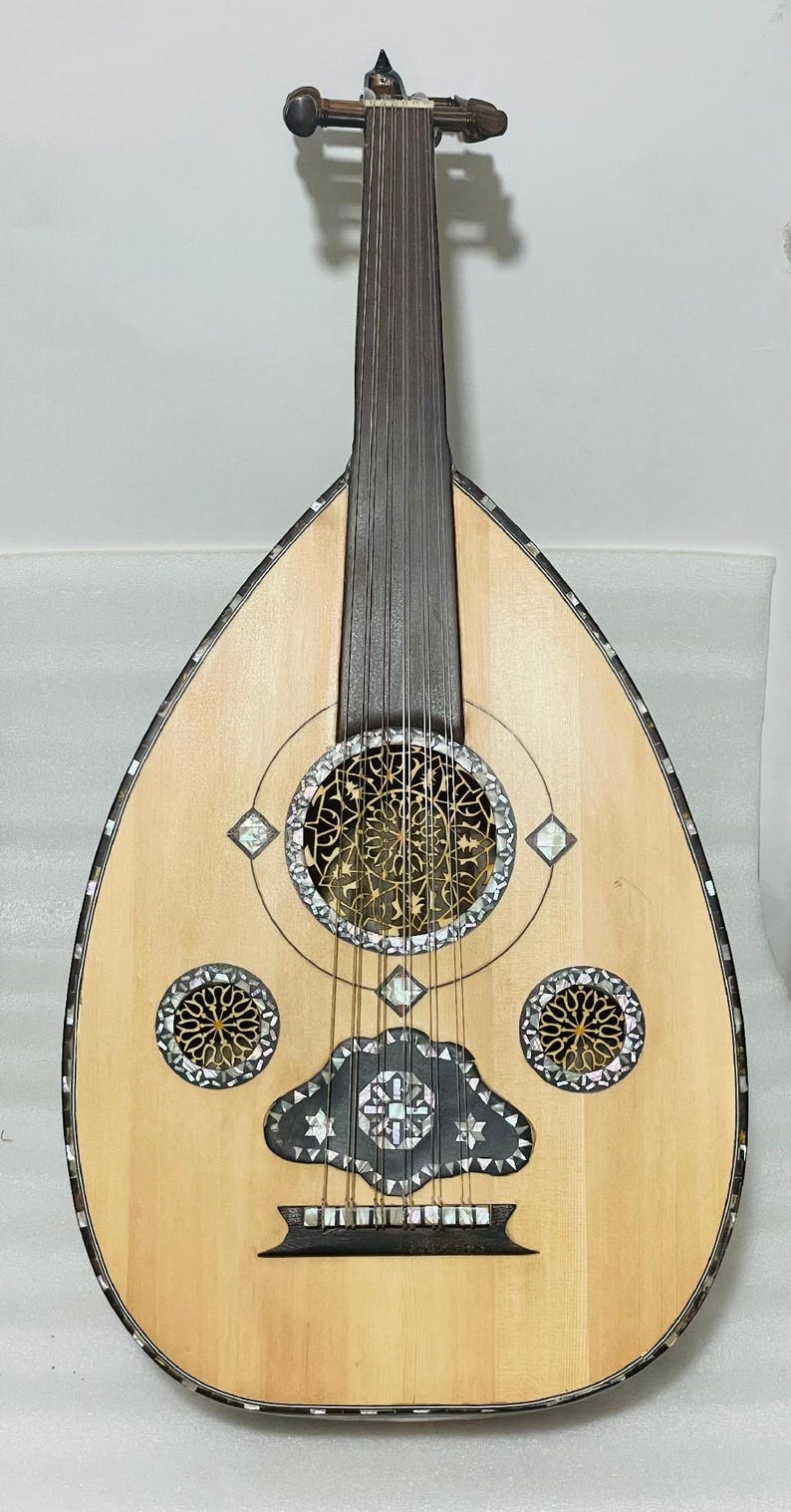 Op de afbeelding: Een lichtgekleurde oed, een snaarinstrument uit het Midden-Oosten, met een peervormige body. Het instrument heeft ingewikkelde inlegwerk van parelmoer rond de klankgaten en randen. De hals en stemschroeven zijn van donker hout.