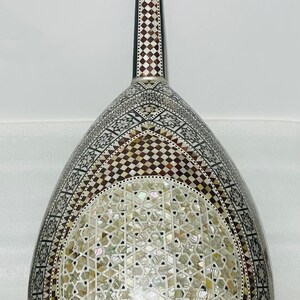Op de afbeelding: Een ingewikkeld versierde oed, een snaarinstrument uit het Midden-Oosten. De peervormige body heeft parelmoer en geometrische patronen in bruin, wit en zwart. De hals heeft stemknoppen en decoratieve inlays.