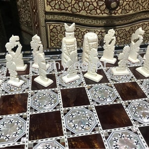 May include: A white bone chess set with intricately carved pieces on a brown and white inlaid chessboard.