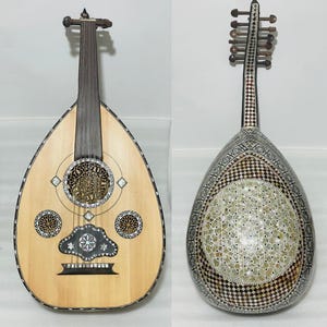 Op de afbeelding: Twee ouds, traditionele snaarinstrumenten uit het Midden-Oosten, worden getoond. E&eacute;n oud heeft een licht houten body met ingewikkeld ingelegd parelmoer en decoratieve klankgaten. De andere oud heeft een donkere, bewerkte body met een vergelijkbaar ontwerp.