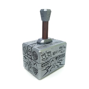 May include: A silver metal replica of Thor's hammer, Mjolnir, with intricate carvings and a brown handle.