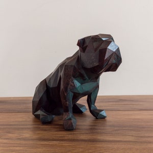 May include: A geometric bulldog sculpture made of dark brown and teal coloured resin. The sculpture is sitting on a wooden surface.