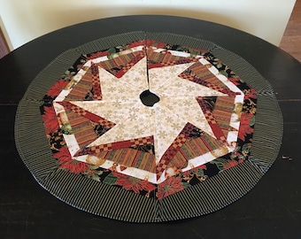 May include: A round, multi-colored Christmas tree skirt with a starburst design in the center. The skirt is made of fabric with a variety of patterns, including stripes, plaid, and floral prints. The outer edge of the skirt is trimmed with a green and white striped fabric.
