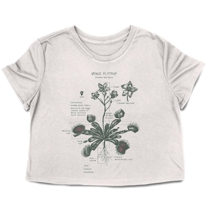 May include: A light gray crop top featuring a detailed botanical illustration of a Venus Flytrap. The graphic includes labeled parts of the plant, such as the flower, leaf, and root system. The text "VENUS FLYTRAP" is printed at the top.