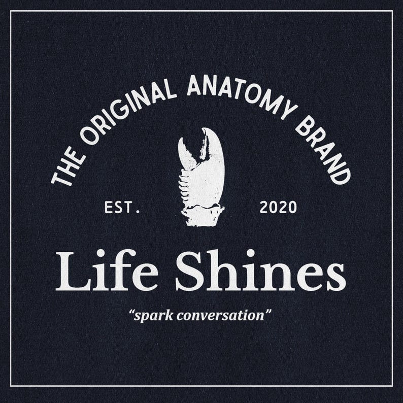 May include: White text on a dark blue background reads "The Original Anatomy Brand Est. 2020 Life Shines "spark conversation"". A white illustration of a lobster claw is centered above the text.