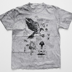 May include: A light grey t-shirt with a black illustration of an osprey, scientific diagrams, and text. The shirt has a textured, distressed look. The design is reminiscent of a vintage scientific study.