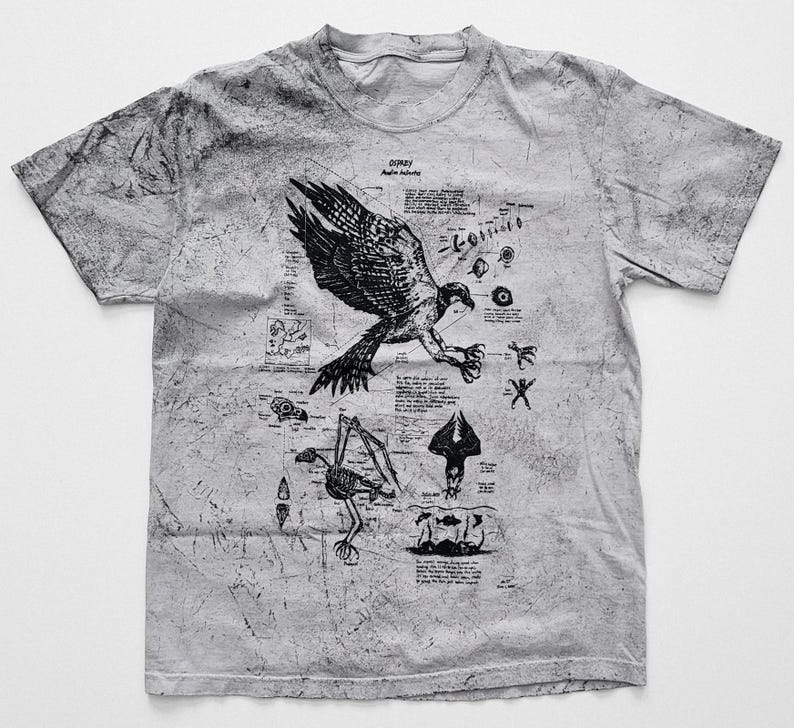 May include: A light grey t-shirt with a black illustration of an osprey, scientific diagrams, and text. The shirt has a textured, distressed look. The design is reminiscent of a vintage scientific study.