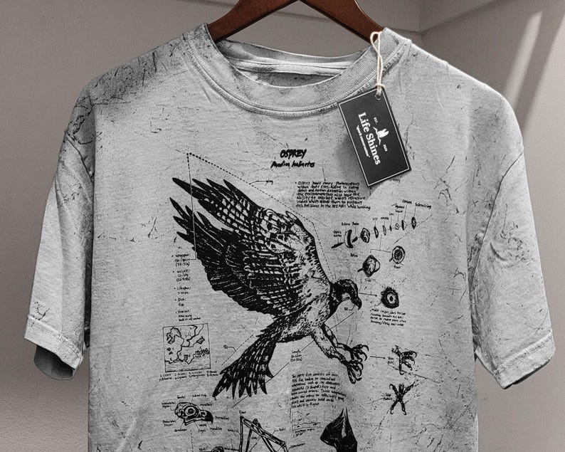 May include: A grey t-shirt featuring a detailed black illustration of an osprey with scientific diagrams and text. The shirt has a distressed appearance and a tag that reads "Life Shines".