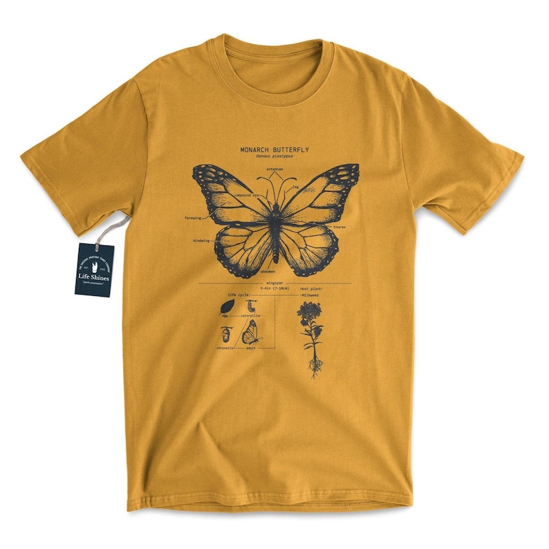 May include: A mustard yellow t-shirt with a black and white illustration of a monarch butterfly and its life cycle. The text "MONARCH BUTTERFLY" and "Danaus plexippus" is printed on the shirt.