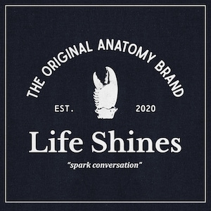 May include: Navy blue graphic design with white text. The text reads "THE ORIGINAL ANATOMY BRAND" in an arch, with a white claw graphic in the centre. Below is "Life Shines" and "spark conversation". Established 2020.