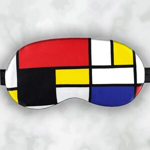 May include: A sleep mask with a Mondrian-inspired design. The mask features a pattern of red, yellow, blue, black, and white rectangles separated by black lines. It has a black elastic strap for securing around the head.