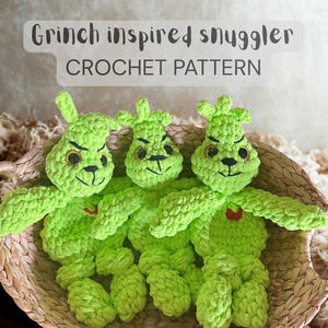 Può includere: Tre pupazzi all'uncinetto verde lime ispirati al Grinch con tratti del viso ricamati in nero e cuori rossi, in un cestino di vimini. Il testo "Grinch inspired snuggler CROCHET PATTERN" è visualizzato sopra.