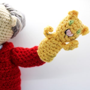 May include: A crocheted puppet with a red jacket and a yellow hand puppet with a green face.
