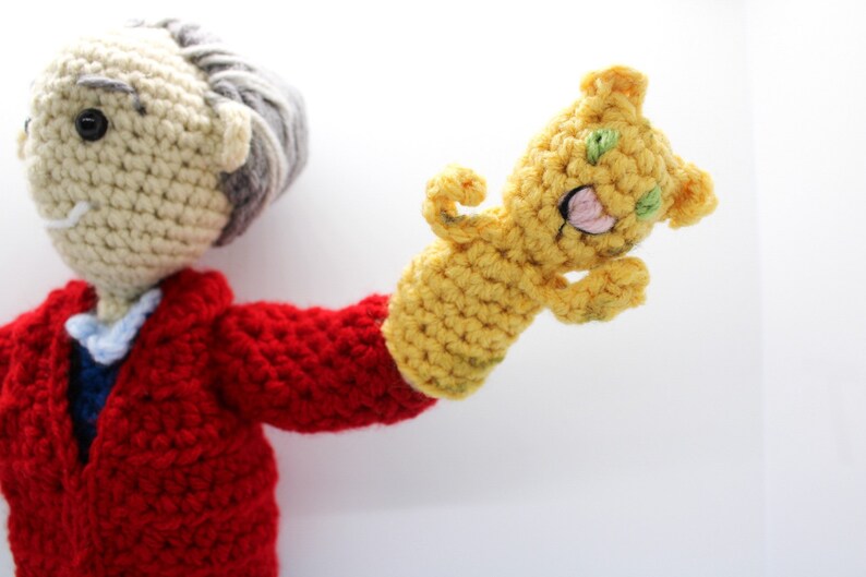 May include: A crocheted puppet with a red jacket and a yellow hand puppet with a green face.